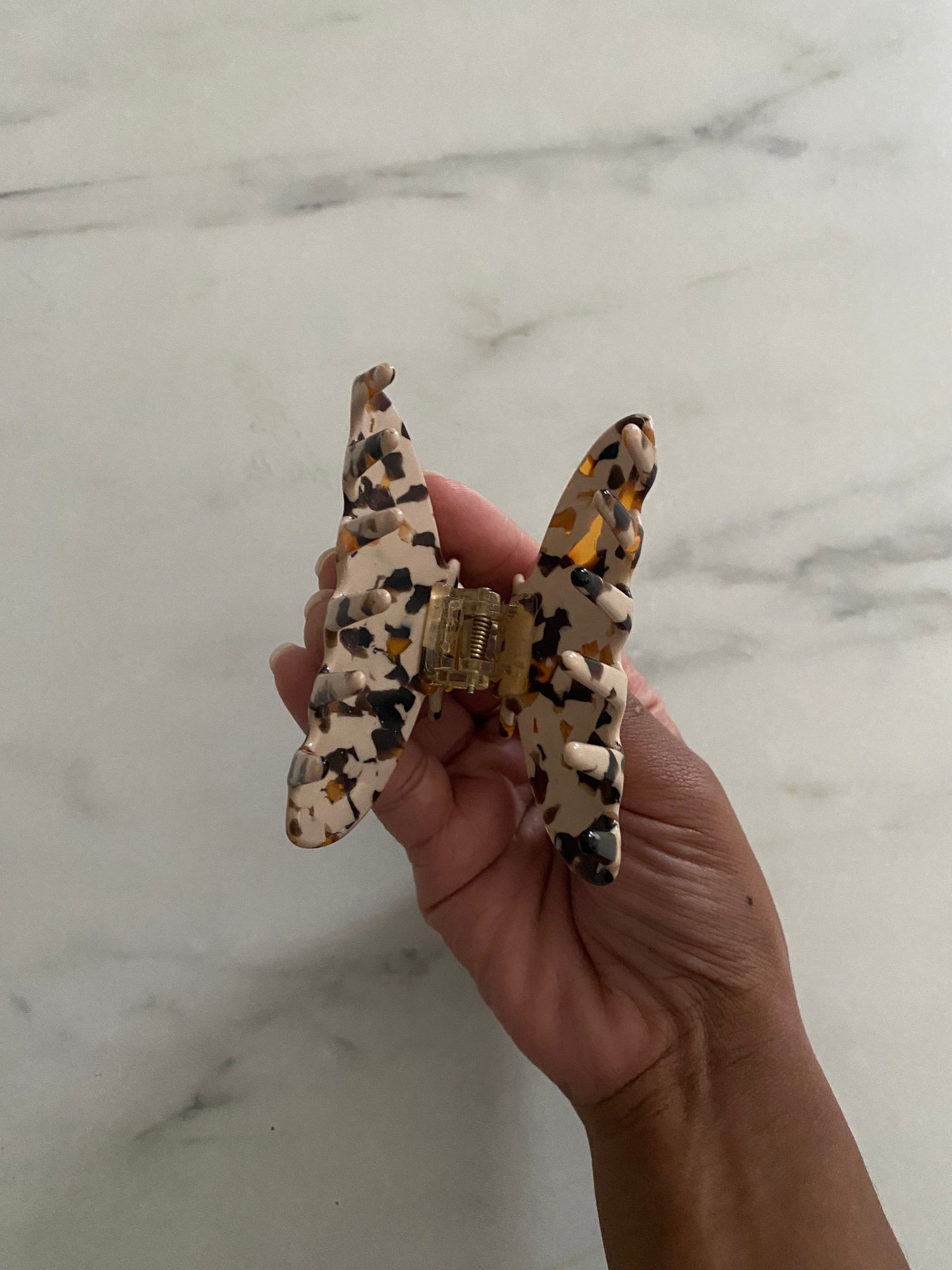 Hand holding a leopard print hair clip against a marble background